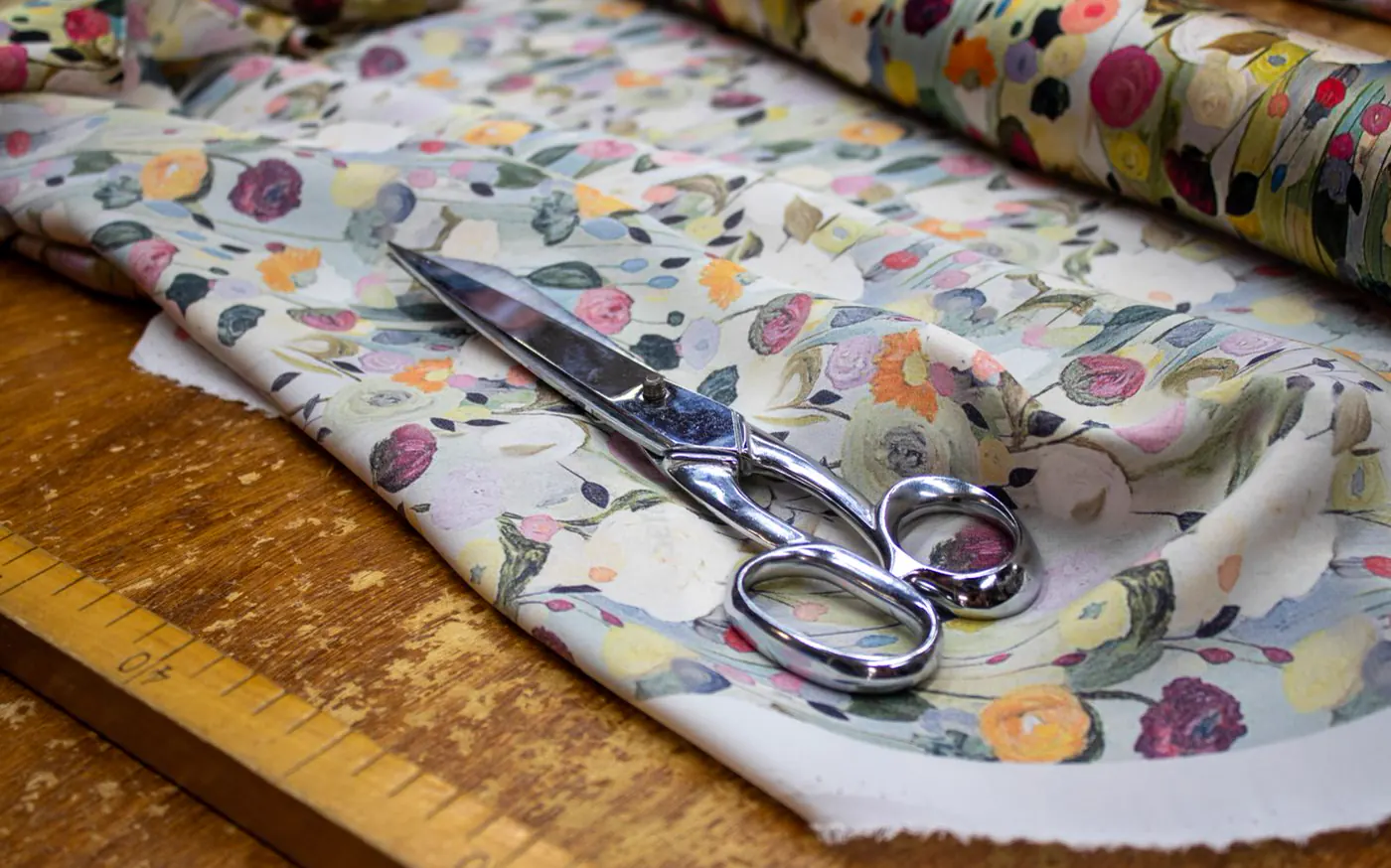 Floral print fabric and sewing scissors on a wooden work table